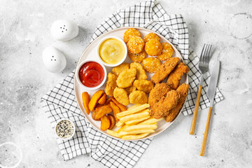Chicken nuggets, strips, french fries, fried potatoes, ketchup and cheese sauce on a light background. Fast food top view 