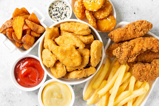 Chicken nuggets, strips, french fries, fried potatoes, ketchup and cheese sauce on a light background. Fast food closeup