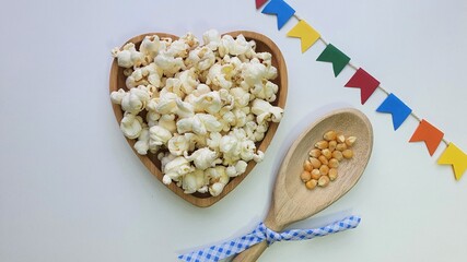 Colorful flags, popcorn in bowl and popcorn kernels in a wooden spoon, on the table. Popcorn, typical June food. Brazilian June Party.