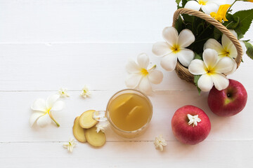 Obraz na płótnie Canvas hot ginger water herbal healthy drinks health care for cough sore with apple, flowers frangipani arrangement flat lay style on background wooden white