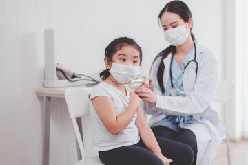 Asian child wearing face mask getting vaccinated during coronavirus or covid-19 pandemic at...