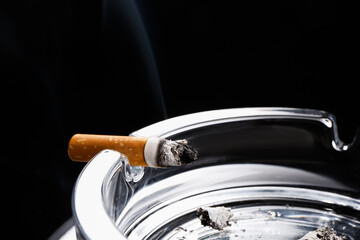 Cigarette and ash tray on dark background, closeup