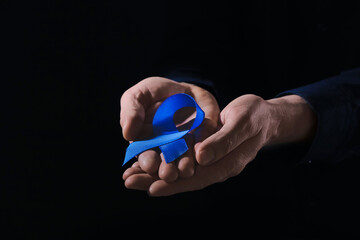 Man with blue ribbon on dark background, closeup. Colon cancer concept
