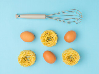 Eggs, pasta and a whisk for whipping on a blue background.