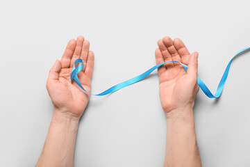 Male hands with blue ribbon on light background. Prostate cancer concept
