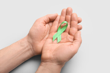 Male hands with green ribbon on light background, closeup. Mitochondrial diseases and kidney cancer concept