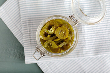 Glass jar with canned jalapeno on color wooden background