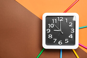 Stylish clock and pencils on color background