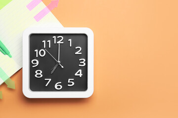 Stylish clock and notebook on color background