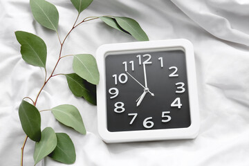 Stylish clock and green branch on bed