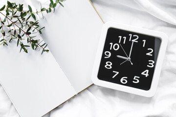 Stylish clock and notebook on bed