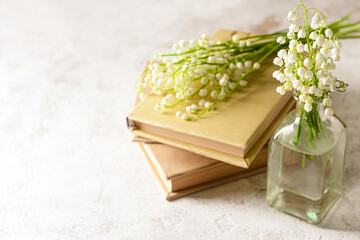 Vase with beautiful lily-of-the-valley flowers and books on light background