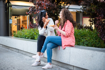 two girls eating pizza in the city two friends sitting eating. Two tourist on the street eating. A lesbian couple eating together