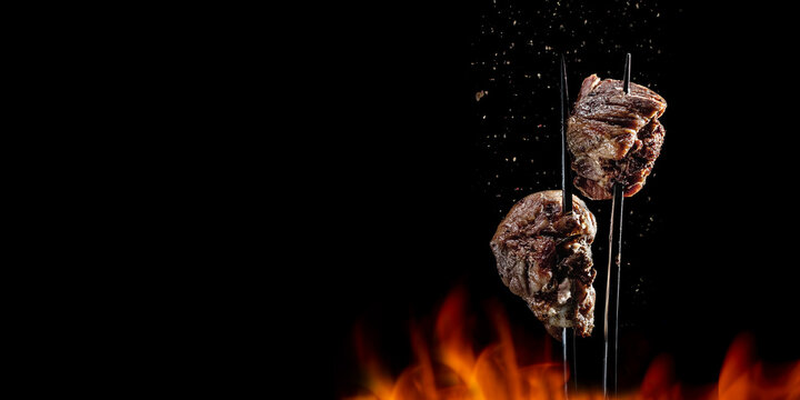 Fork with pieces of delicious barbecued meat on black background. Delicious pork pieces on rotating fork close-up. Grilled cubes of pork meat on fork. Tasty meat. Space for text. Long wide banner