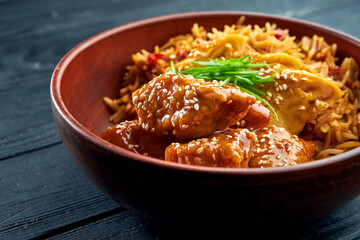 Pan-Asian Street Food - Sweet and Sour Chicken Garnished with Rice, served in a bowl on a wooden background. Wok rice with chicken. Asian food. Selective focus