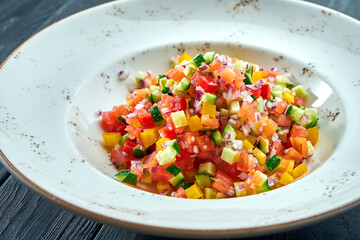 Vegetable salad with tomatoes, peppers, cucumber and onions in a white plate on a dark wood background. Veggie salad