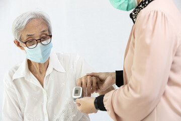 Female caregiver with fingertip pulse oximeter,attached on finger of elderly,health check,measuring oxygen saturation level and rate of the heartbeat at home during COVID-19 or Coronavirus pandemic
