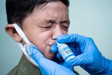 Head shot of child with medical face mask getting Intranasal Coronvirus covid-19 vaccination through nostril from doctor - concept of covid nasal vaccine - obrazy, fototapety, plakaty