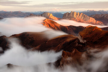 Mountains in fog at sunset in autumn. Landscape with alpine mountain valley, low clouds, forest,...