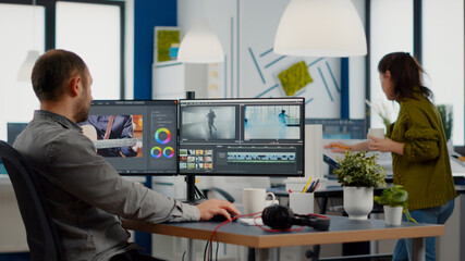 Videographer edits video project and cuts footage and sound using post production software and two...