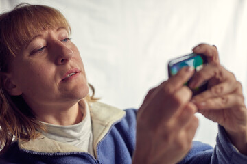 Fototapeta premium Portrait of a middle-aged woman with cell phone on a white background. Unprofessional female model doing selfie in the room or in the Studio