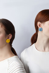 Cropped shot: two ladies are showing funny asymmetric earrings made as characters of...