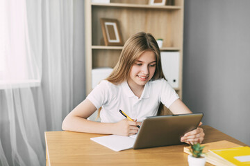An attractive student is studying an online course and taking notes while preparing for the exam with a tablet. The concept of education and upbringing, preparation for exams