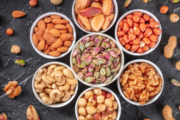 Nuts in bowls and scattered, top shot on a black background. Pistachios, peanuts, walnuts and other vibrant nuts