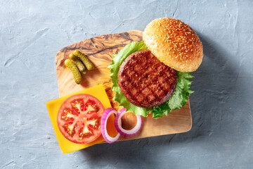 Burger ingredients, shot from the top on a wooden board. Beef patty with green salad, tomato,...
