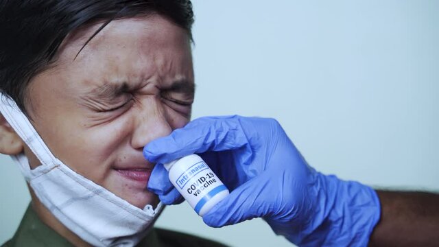 Head Shot Of Young Little Child With Medical Face Mask Getting Intranasal Coronvirus Covid-19 Vaccination Or Jab Through Nostril From Doctor - Concept Of Covid Nasal Vaccine.