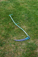 A hand scythe lies on the lawn on a summer day