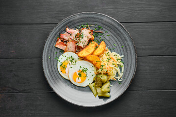 Overhead view of fried eggs, ham with potato wedges, pickled cabbage and cucumber