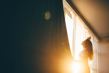 Woman standing near big window at sunrise.