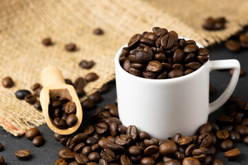 Coffee beans roasted in a wooden cup with a wooden scoop and a white coffee cup were placed on a sackcloth on a black stone floor.