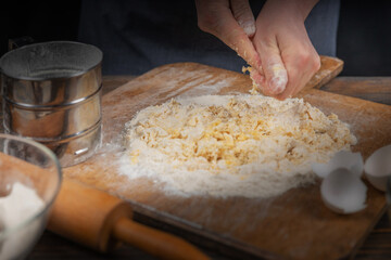 Women's hands, flour and dough. A woman in an apron prepares dough for homemade baking, a rustic home cozy atmosphere, a dark background with unusual lighting.
