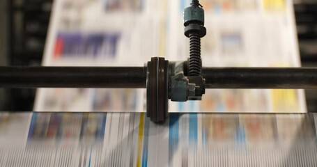 Newspaper runs through a roll machine parallel to the camera view with two layers of focus revealed during the clip
