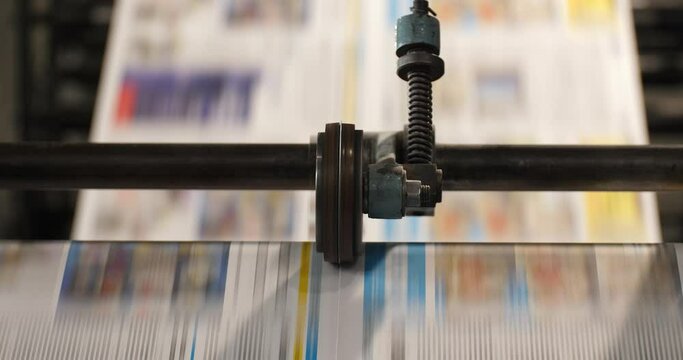 Newspaper runs through a roll machine parallel to the camera view with two layers of focus revealed during the clip