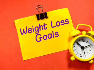 Healthcare concept. Text Weight loss goals on colorful paper note with clock on red background.