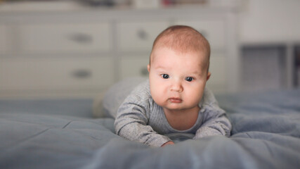 Cute bald baby 2 3 months old lies on the bed on his stomach, close-up, toning