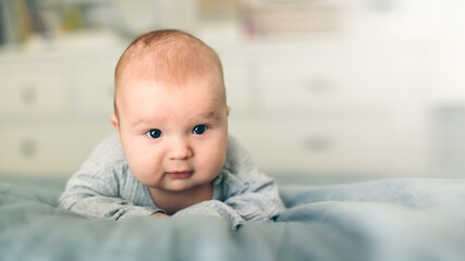 Cute bald baby 2 3 months old lies on the bed on his stomach, close-up, toning