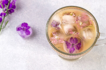 Obraz na płótnie Canvas Glass with cappuccino coffee and ice cubes with purple flowers