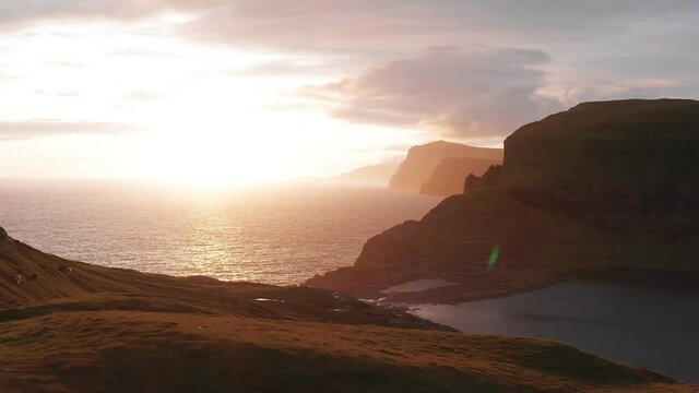 Aerial view of beautiful orange sunset in Faroe Island. Huge cliff and sea stacks glow in golden evening light