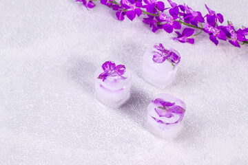 Obraz na płótnie Canvas Purple flowers frozen in ice cubes on light gray background with copy space