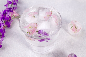 Glass with lemonade and ice cubes with purple and soft pink flowers