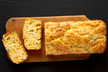 Homemade Cheesy Bread Loaf on a rustic wooden board on a black background, top view. Flat lay, overhead, from above.
