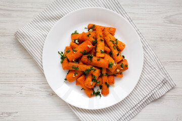 Homemade Roasted Carrots with Herbs on a white plate on a white wooden table, top view. Flat lay,...