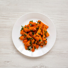Homemade Roasted Carrots with Herbs on a white plate on a white wooden surface, top view. Flat lay, overhead, from above.