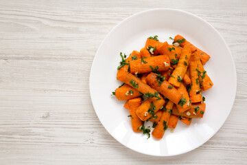 Homemade Roasted Carrots with Herbs on a white plate on a white wooden background, top view. Flat lay, overhead, from above. Copy space.