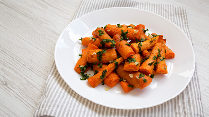 Homemade Roasted Carrots with Herbs on a white plate on a white wooden background, side view. Copy space.