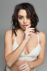 Naklejka premium Sensual woman in bra holding hand near mouth isolated on grey